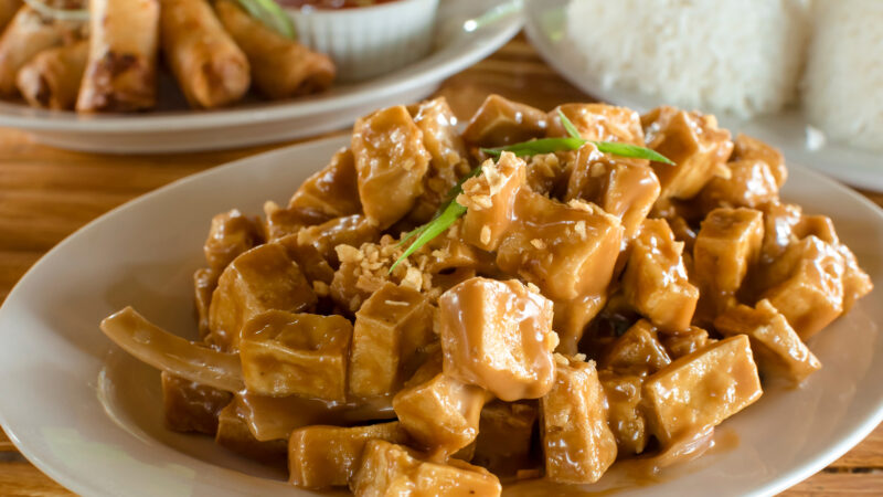 Sizzling tofu, with Lumpiang Shanghai and a cup of rice. Philippine cuisine enjoyed outdoors in a traditional setting.